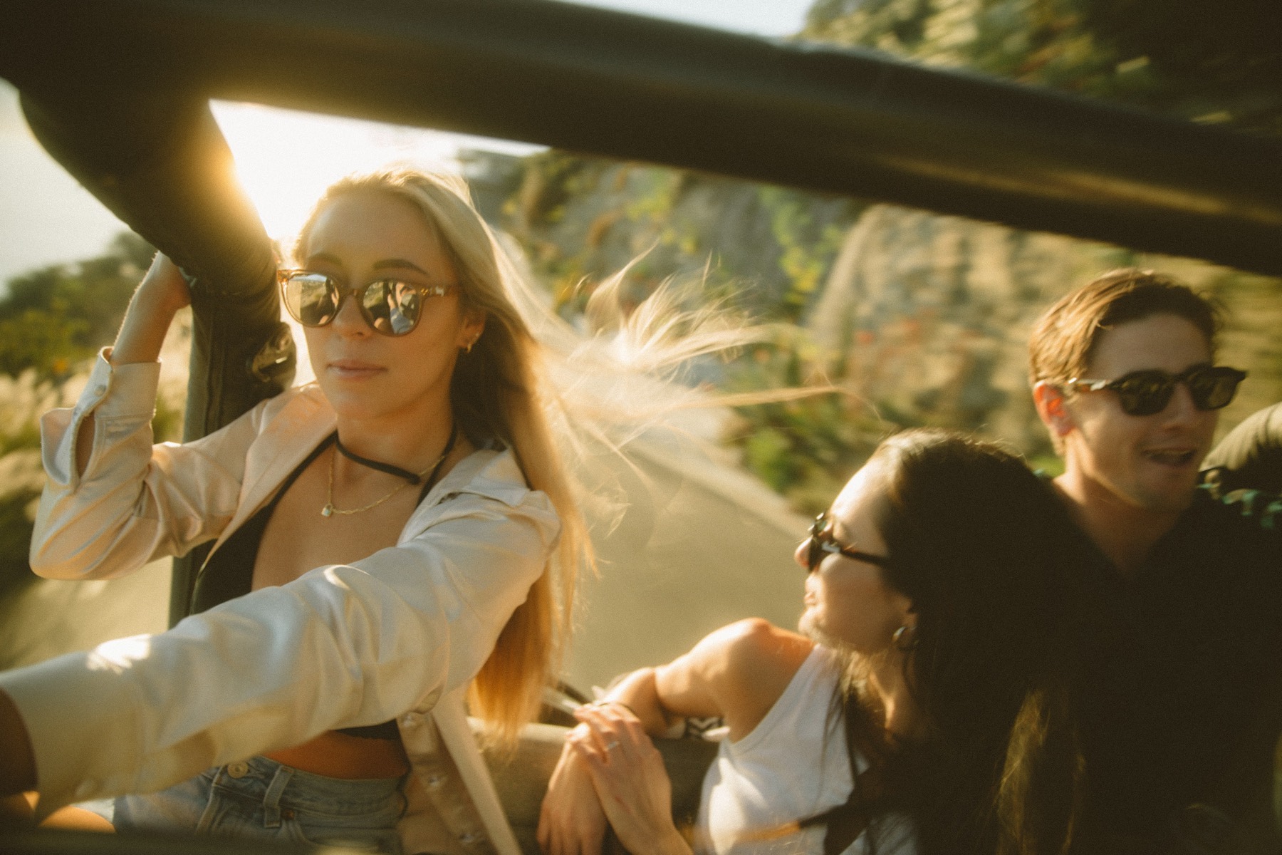 Three friends laughing together in an open-top car at golden hour