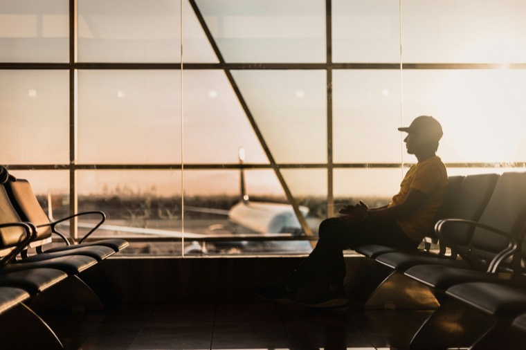 Traveller waiting at an airport gate window at sunset, with a plane outside